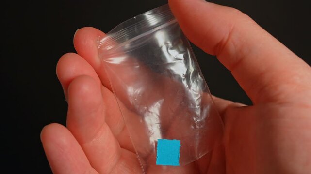 Drug dealer with LSD acid paper squares packed in small bag for sale, controlled drugs. Hallucinogenic psychedelic substances used in party and dance clubs.