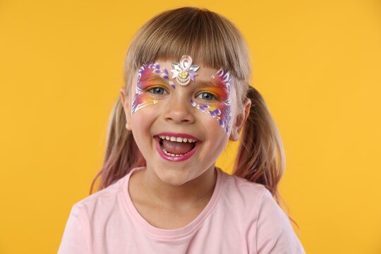 Little girl with beautiful face painting on orange background