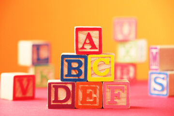 Wooden cubes with letters on pink table against orange background, closeup