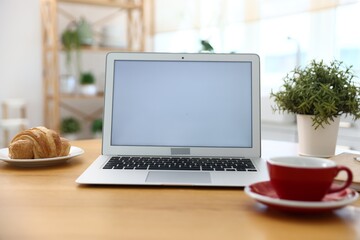 Fototapeta premium Workplace with laptop, cup, croissant and decor on wooden table indoors