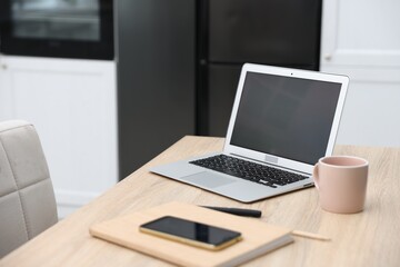 Fototapeta premium Workplace with laptop, stationery, smartphone and mug on wooden table indoors