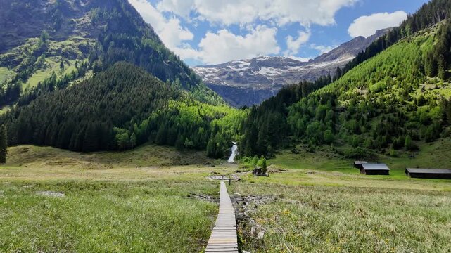 Wooden path through marshy terrain to river. Mountain landscape with waterfall river. Mountain landscape bridge path. Village landscape. Picturesque valley with waterfall coming down from mountain