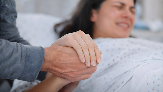 Pregnant woman experiencing contraction on hospital bed while partner supports her holding hand. Husband comforting wife during labor. Care and emotional support during childbirth

