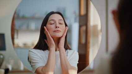 Obraz premium Brunette performing facial massage looking mirror at beauty ritual home closeup.