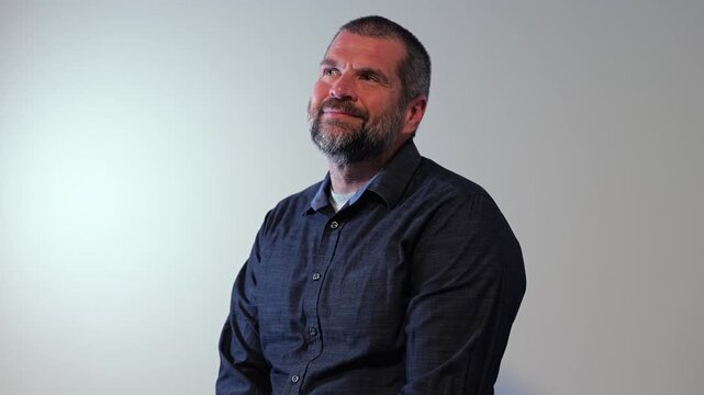 Confident middle-aged man with beard wearing a dark button-down shirt posing against a neutral backdrop, representing modern business leadership