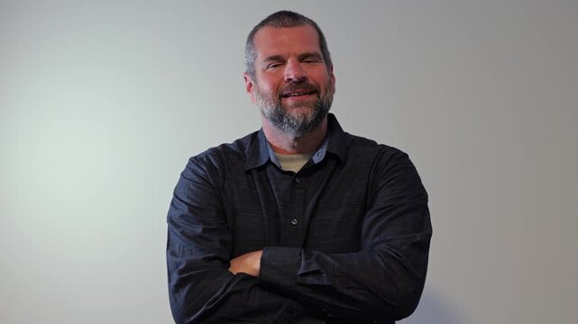 Confident middle-aged man with beard wearing a dark button-down shirt posing against a neutral backdrop, representing modern business leadership