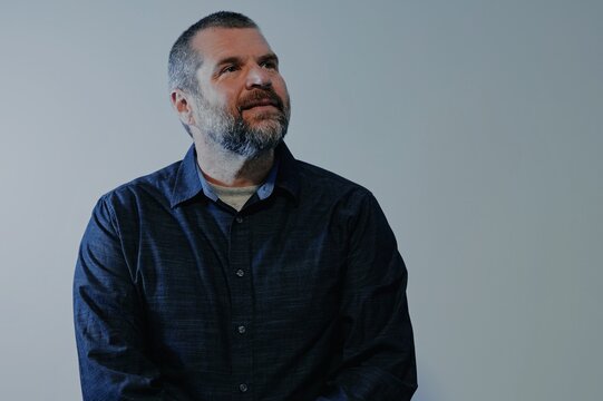 Confident middle-aged man with beard wearing a dark button-down shirt posing against a neutral backdrop, representing modern business leadership