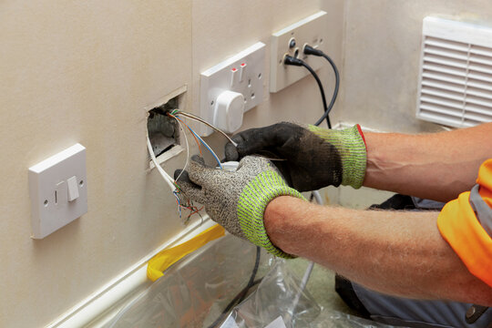Telecoms engineer in gloves removing copper wiring from UK telephone socket back box