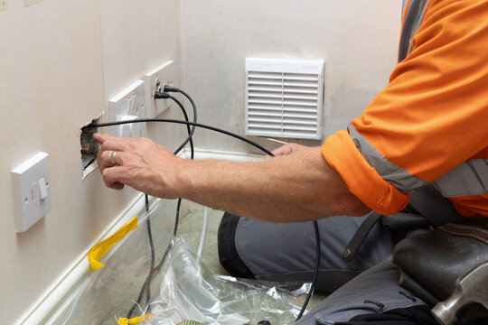 Telecoms engineer feeding fibre optic cable through wall cavity during broadband upgrade