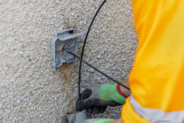 Telecoms engineer feeding fibre cable into exterior wall entry bracket on pebbledash wall © Tosh Lubek