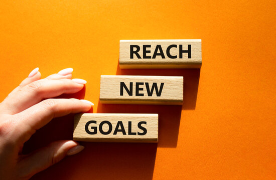 Concept words reach new goals on wooden blocks arranged as steps. Businessman hand arranging wooden blocks. Goal achievement and personal development concept. Orange background. Copy space.