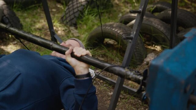 Young adult Caucasian man performing bench press on homemade outdoor gym equipment. Footage suitable for fitness, healthy lifestyle, and budget workout marketing campaigns