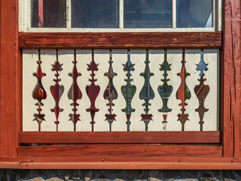 Carved Wooden Balcony Railing With Decorative Cutouts and Red Trim Under Window