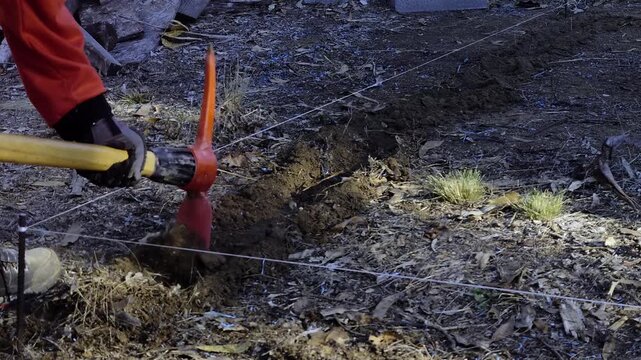 Worker Digging Foundation Hole with Pickaxe, Ground Excavation for Construction Project, Manual Labor, Site Preparation and Earthmoving Outdoors