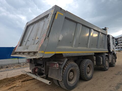 Heavy Dump Truck at Urban Construction Site Rear view of a rugged dump truck parked on a muddy urban construction site beneath dramatic cloudy skies.