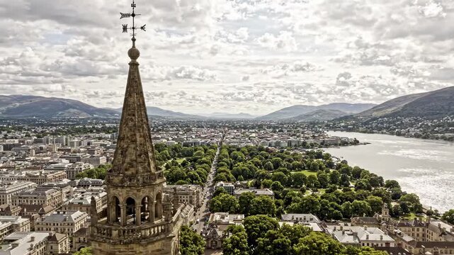 Aerial view of a historic church spire overlooking a city with a river and mountains in the background
