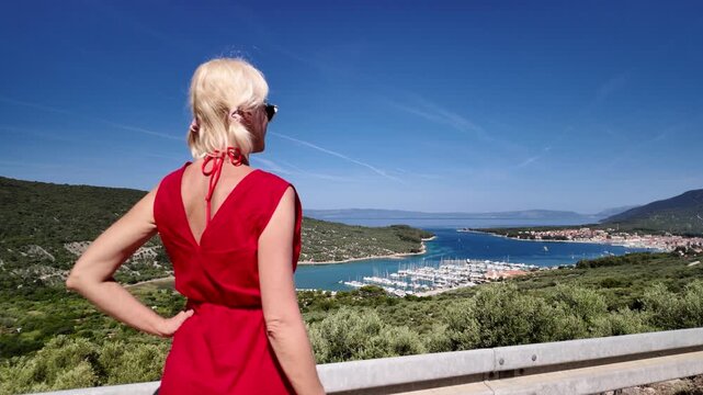 Young woman relaxing by panorama overlooking the historic town of Cres harbor during a sunny summer day of Cres Island in Croatia