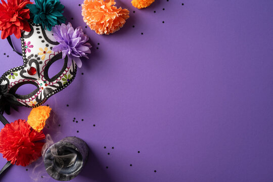 Colorful Day of the Dead mask with marigolds, incense and confetti on purple background