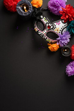 Decorative sugar skull mask with marigolds and candles for Dia de los Muertos celebration on black vertical background