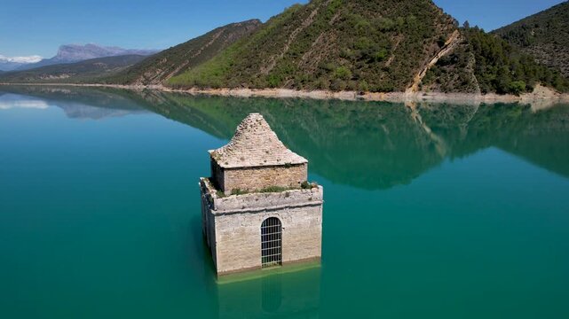 Orbital aerial footage of Asunci&oacute;n de Mediano Church covered with water of Mediano Reservoir on sunny spring day. Huesca, Spain.