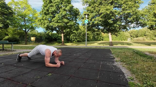 Man in his 50s performing bodyweight exercises at an outdoor fitness park on a clear day. Healthy lifestyle, fitness, strength, endurance, active aging, and outdoor physical activity.