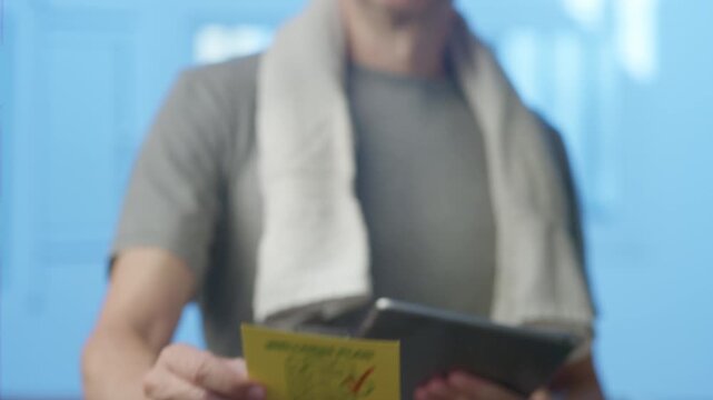 Sporty man with a towel using a tablet while applying a wellness plan sticker on a glass surface, emphasizing a healthy lifestyle combining exercise, rest, and proper nutrition