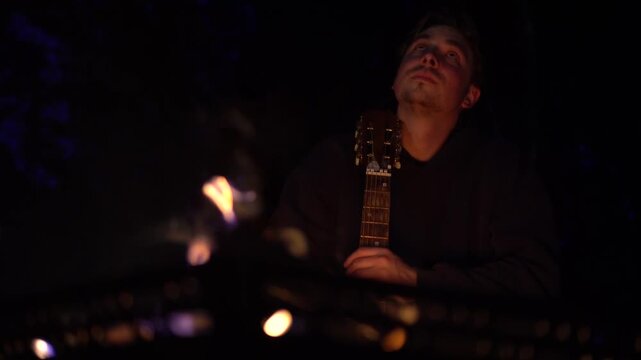 Young Traveler Relaxing with Guitar by Campfire in Night Forest