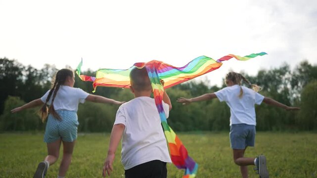 Children run in a field. Group kids play with colorful kite. Children run in nature summer sunlight. Group children run happily. Children enjoy active play outdoors. Childhood joy in group activities.