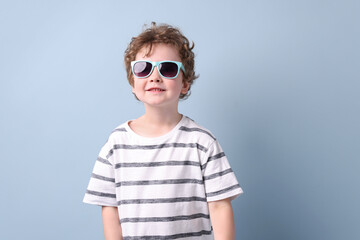 Fototapeta premium Smiling little boy in stylish sunglasses on grey background. Space for text