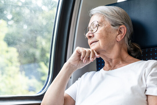 Senior woman with gray hair traveling by train, looking out the window, reflecting on memories or contemplating future plans during a relaxing journey