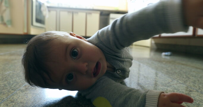 Casual authentic scene of baby infant on kitchen floor wanting to touch camera lens