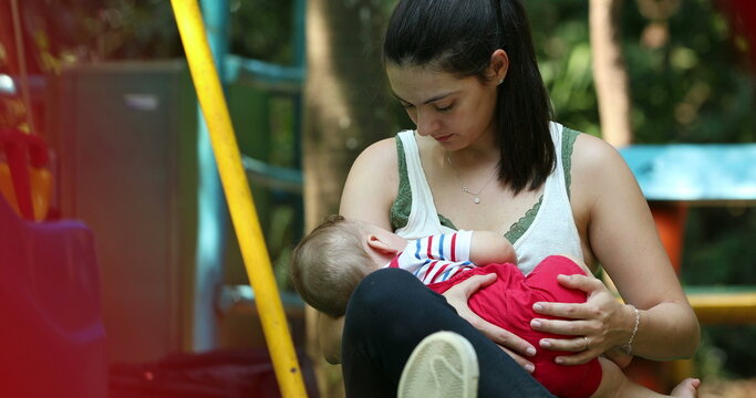 Casual candid mother breastfeeding baby son outside at park