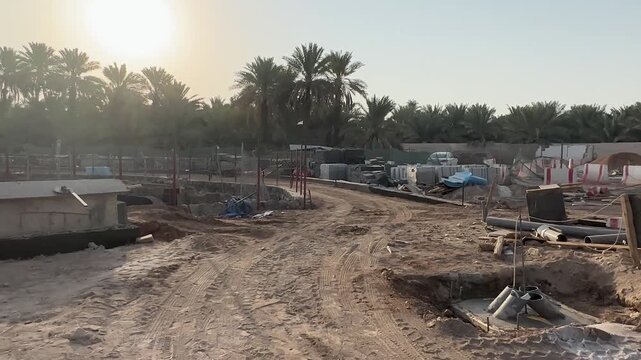 Active construction site near ancient ruins and palm oasis at sunset.