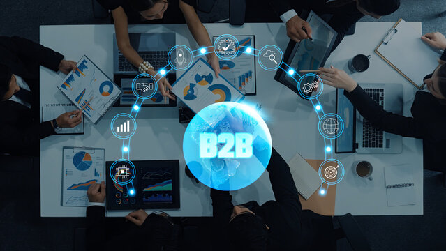 A group of professionals engages in teamwork around a conference table, analyzing charts and data in a modern office setting, highlighting B2B collaboration and strategy. Trope