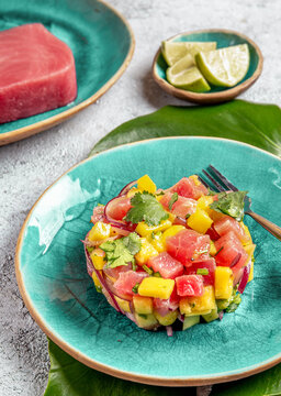 Tropical style gourmet tuna mango salad tartar with cilantro and purple onion. On blue plate, tropical leaves