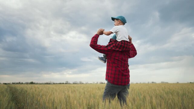 Father carries son on shoulders in field. Family enjoying dream moment. Father son bonding in nature. Happy dream in field. Rural family lifestyle. Dreamy family scene nature. Family values and dreams