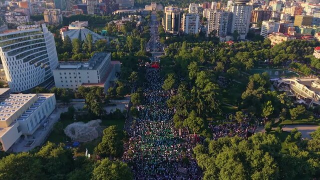 Aerial view of a massive crowd gathering for Eid Mubarak morning prayers in a beautiful park in Tirana, Albania, during the sunrise golden hour.