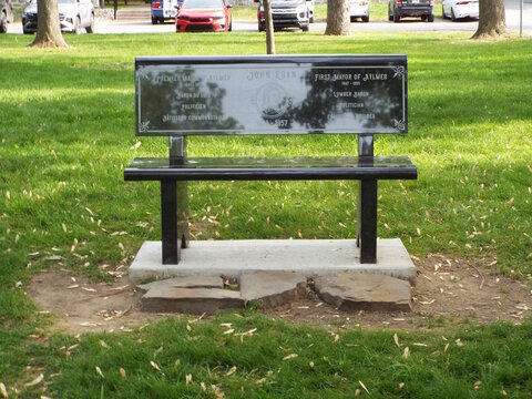 Gatineau,Quebec, Canada &ndash; June 2, 2026: The polished black granite memorial bench honoring "John Egan" features bilingual English and French inscriptions set outdoors in a green park on Rue Principale