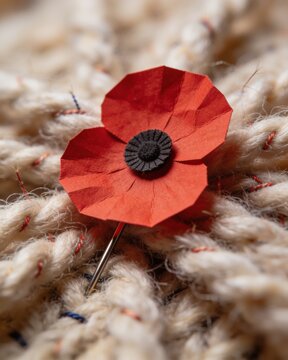 A detailed close-up of a red paper poppy pin inserted into a thick, rustic braided white wool texture, representing a Remembrance Day symbol.