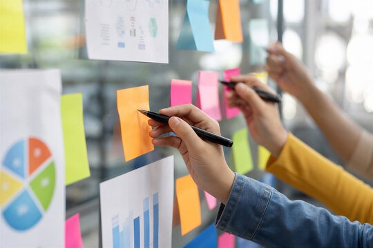 Professionals Brainstorming Ideas and Organizing Concepts with Sticky Notes on a Glass Board During a Collaborative Session.
