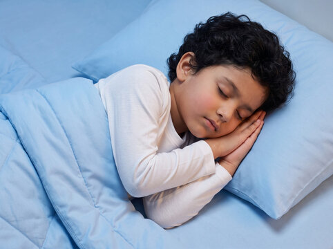 young fair skinned indian boy peacefully sleeping on luxury sky blue bedding at night in side profile representing healthy child sleep parenting pediatric wellness and bedtime routine