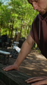 Vertical video of young adult Caucasian man doing push-ups on wooden bench at outdoor gym. Footage ideal for promoting outdoor fitness programs and healthy lifestyle apps