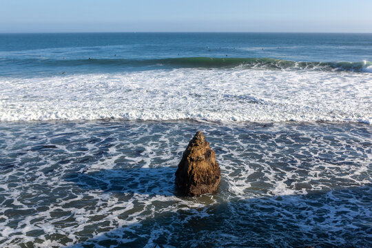 A lone rock formation stands amidst the crashing waves of the Pacific Ocean at Natural Bridges State Beach in Santa Cruz, California, USA.