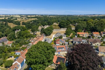 Aerial view of Pickering Castle in North Yorkshire overlooking the historic market town with medieval stone walls surrounding woodland residential homes and rolling countryside beneath clear blue sky © Duncan