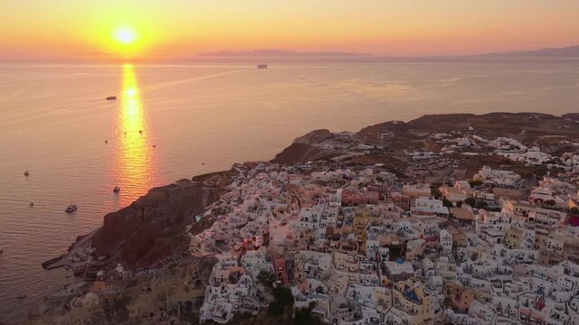 Stunning drone of bright sunset flare over Aegean Sea and Oia historic village cliffside in Santorini Greece