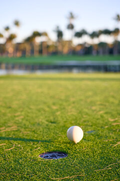 Close up view of a white golf ball resting beside the hole on a green putting surface