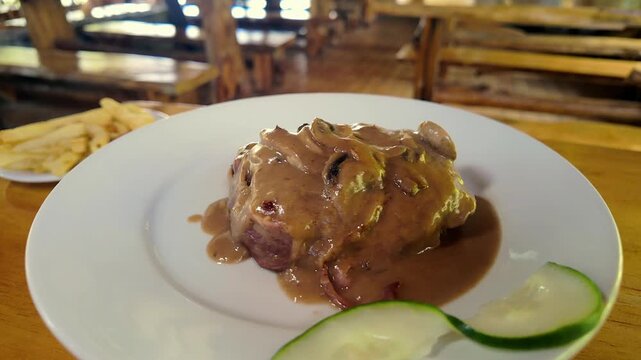 close up of grilled filet mignon steak with mushroom gravy and cucumber garnish on white plate