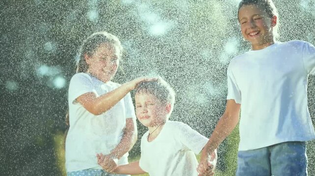 Children playing in rain at park. Happy children splashing in puddle holding hands. kids enjoying rainy day. Fun family time outdoors. Playful childhood moments in nature. Children rain puddle park.