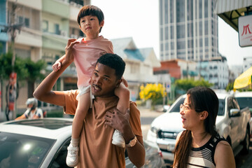 Obraz premium Diverse family enjoying urban stroll, father carrying child on shoulders