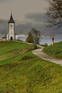 Gold-color dressed girl facing the St.Primus and Felician church (Cerkev svetega Primoža in Felicijana) on a cloudy autumn sunset. Jamnik-Slovenia-171